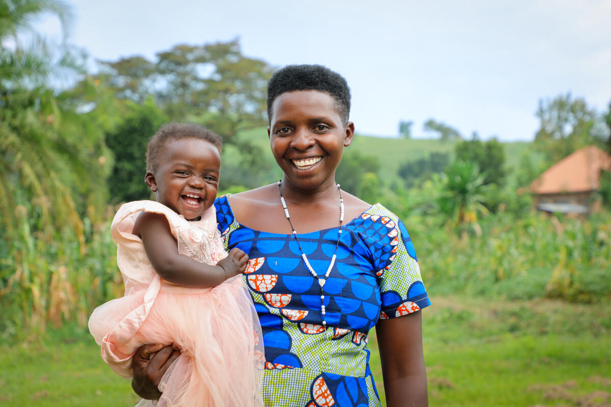 Gloria and her young daughter smiling outside the health centre where there is now running water