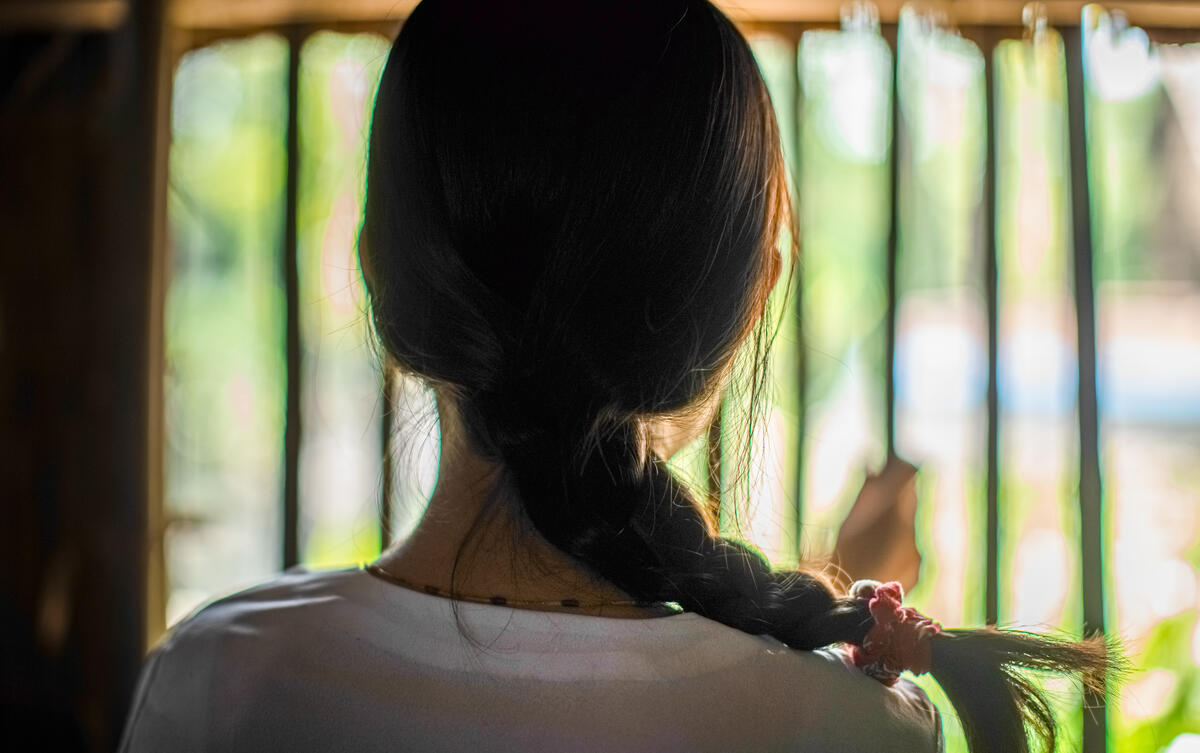 Back of girls head, with metal bars and greenery in background