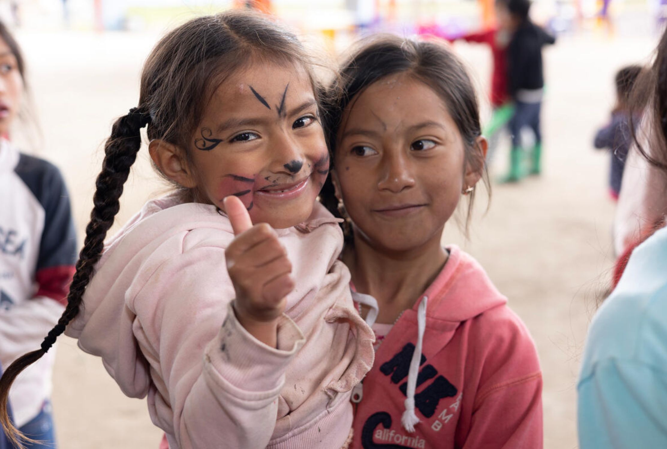 Two smiling young girls from Ecuador, one with her face painted and giving a thumbs up.