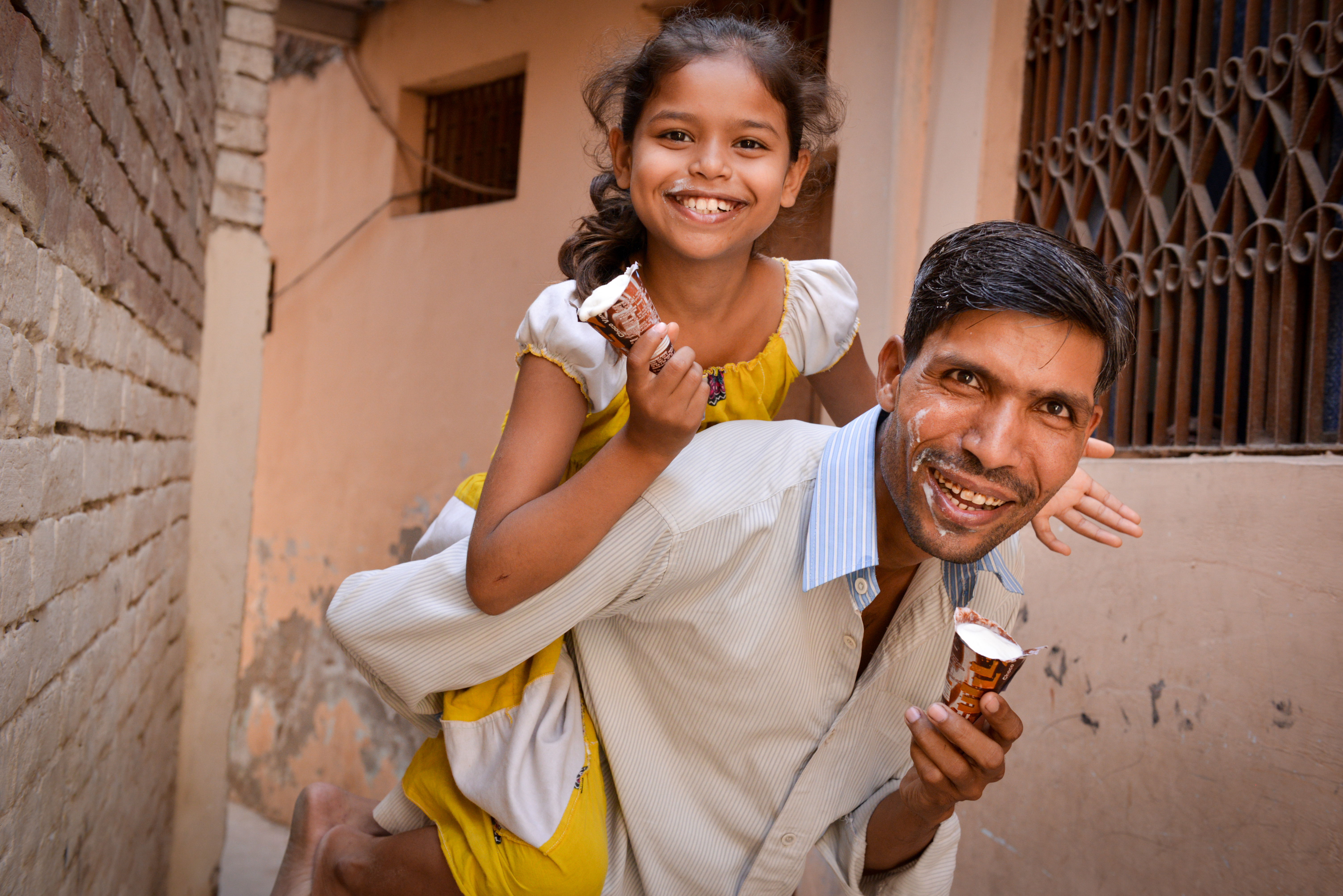Man and his daughter smile as they eat ice cream and he gives her a piggy back