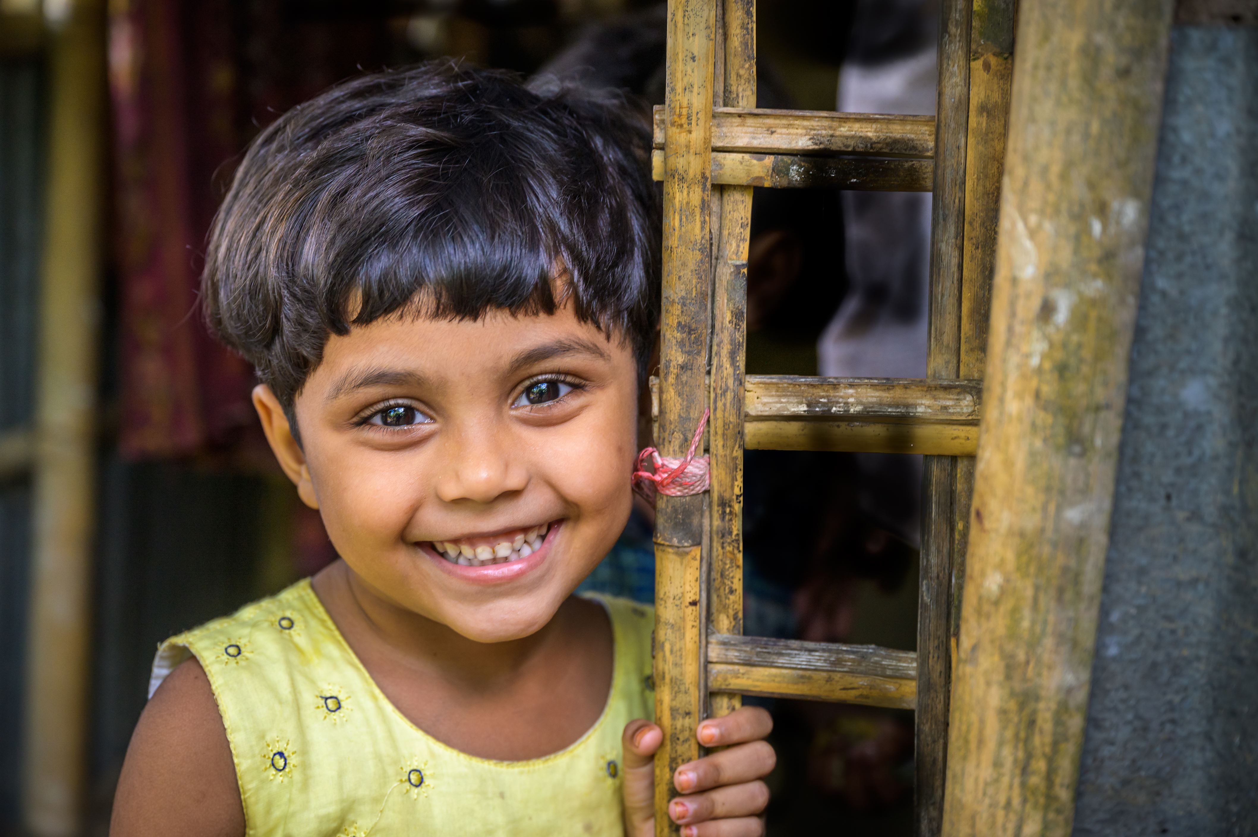 Girl in yellow smiles as she leans against the structure of her house