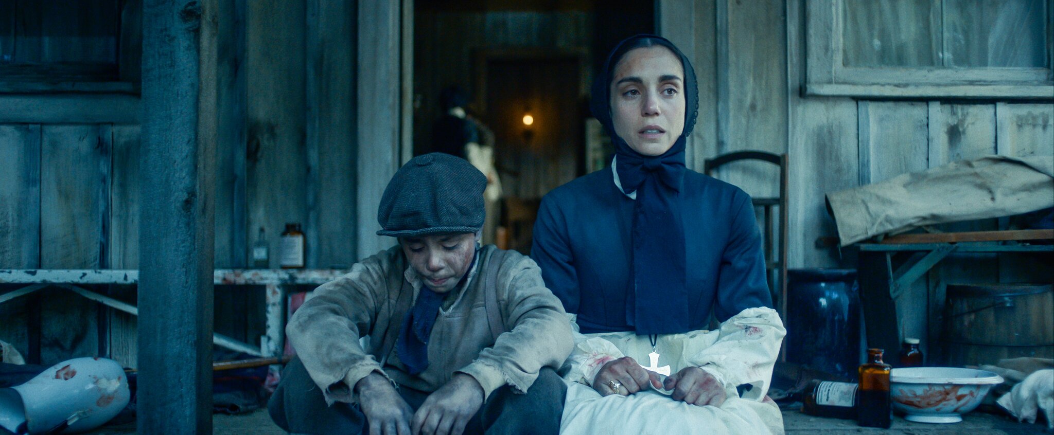 A still from the film showing Cabrini sitting on the steps of a house with a young boy sat beside her