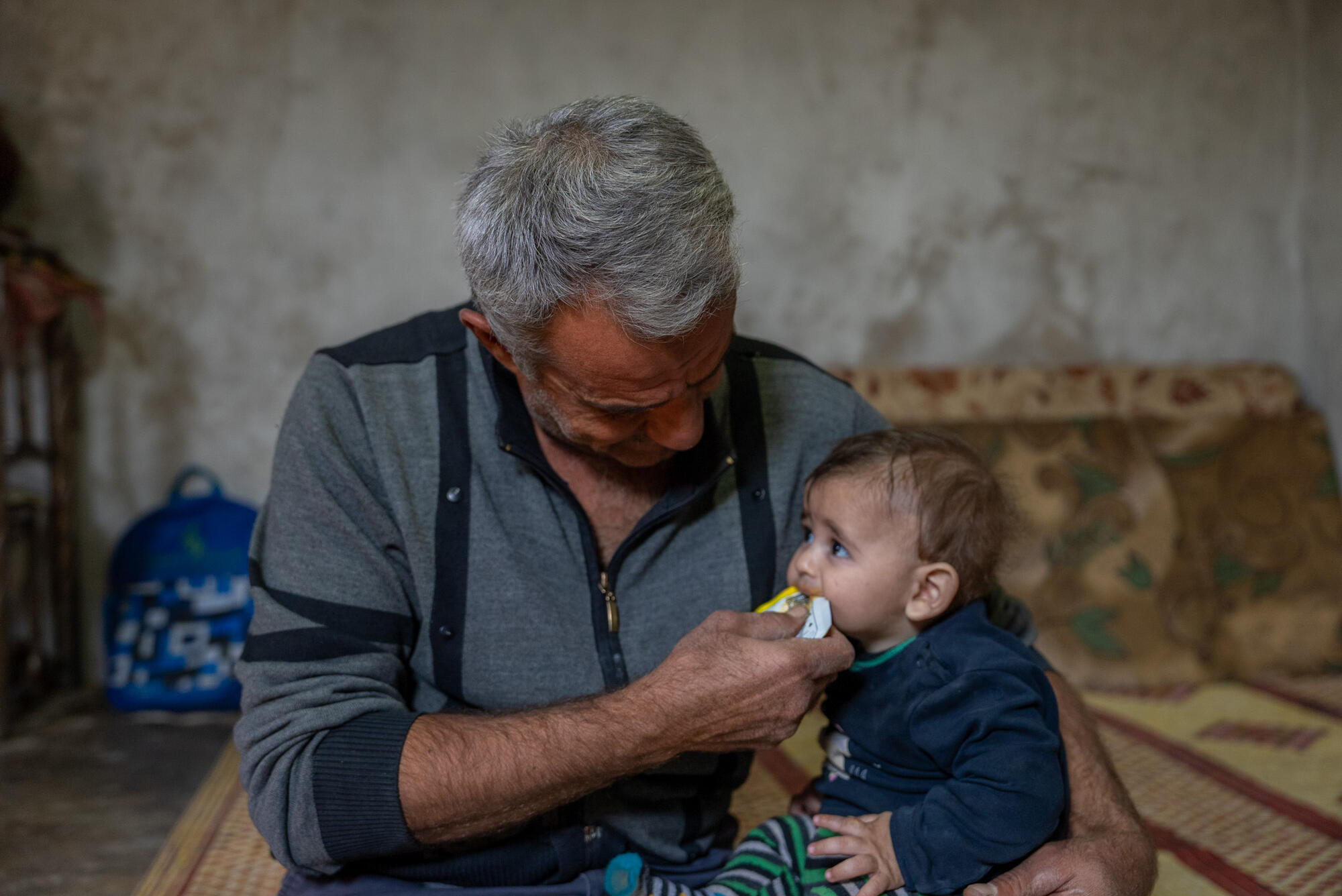 A young child sits on a caregiver's lap being fed