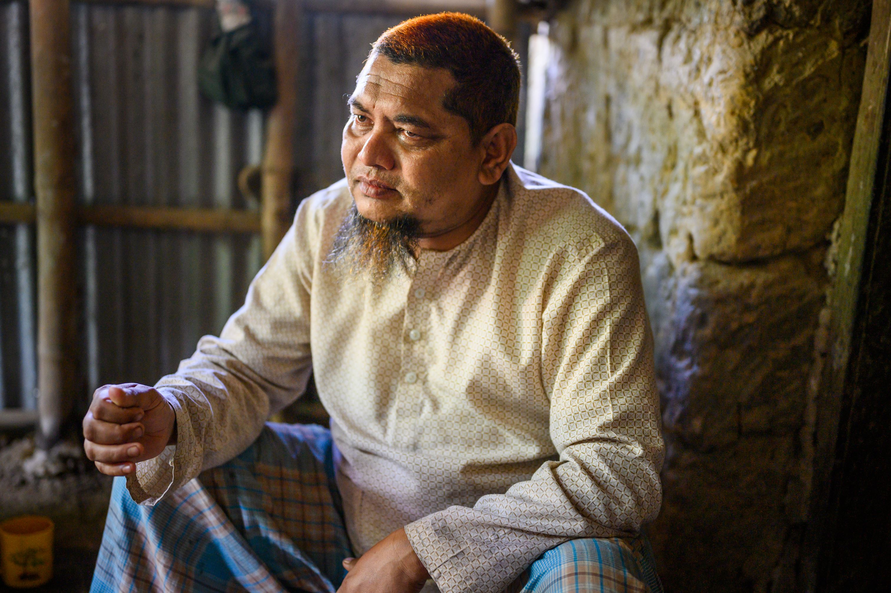 Bangladeshi man in long-sleeved top sits in his house