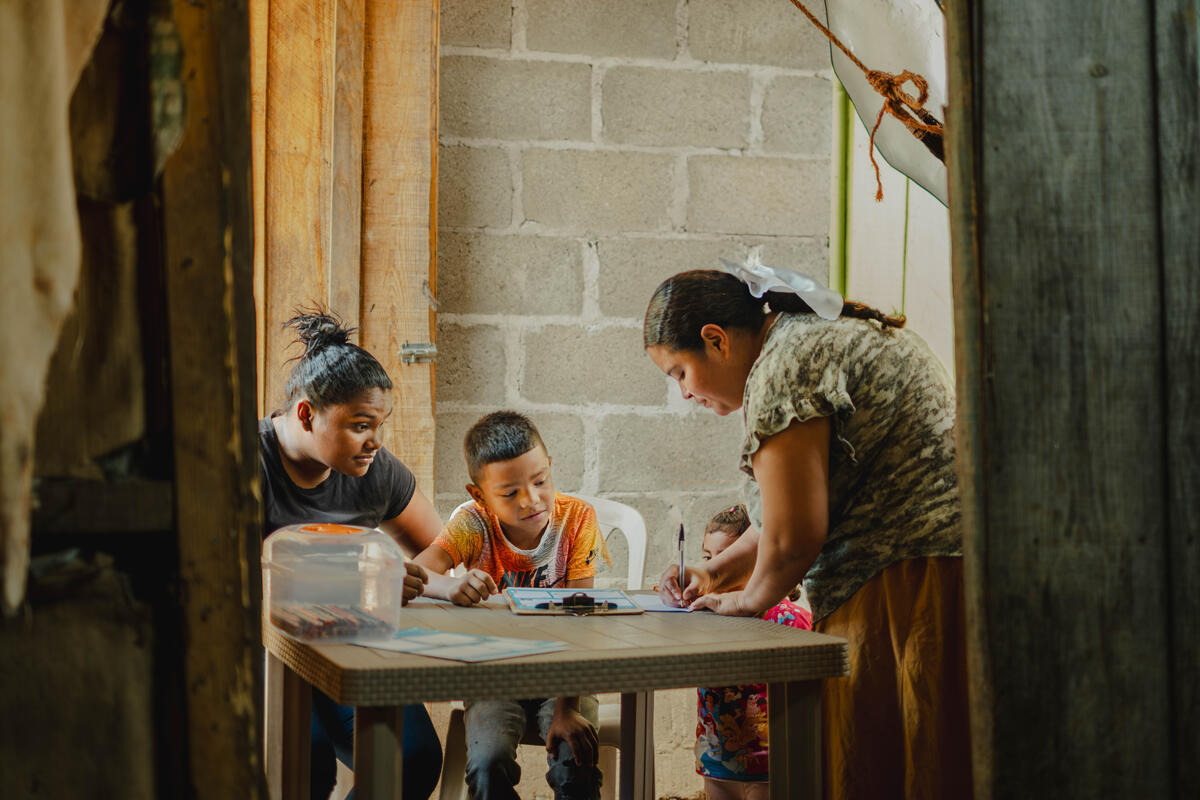 Elisabeth is hunched over a table and there are three children around the table watching her.