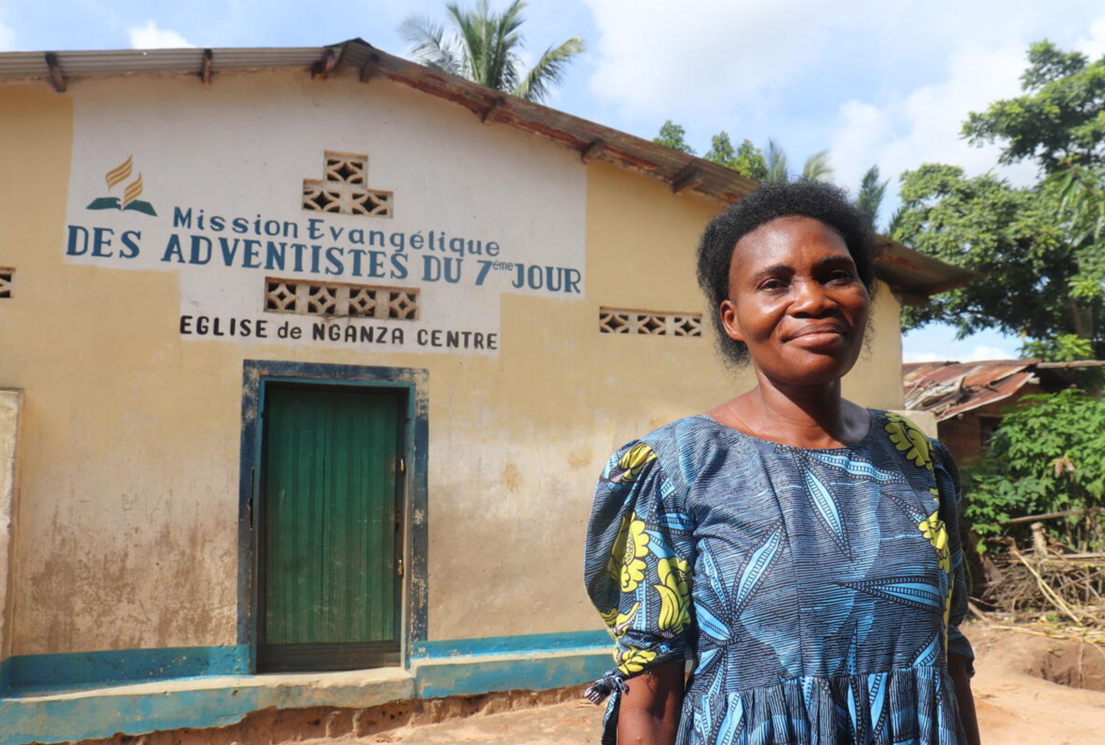 A woman in DRC smiles at the camera in front of a church