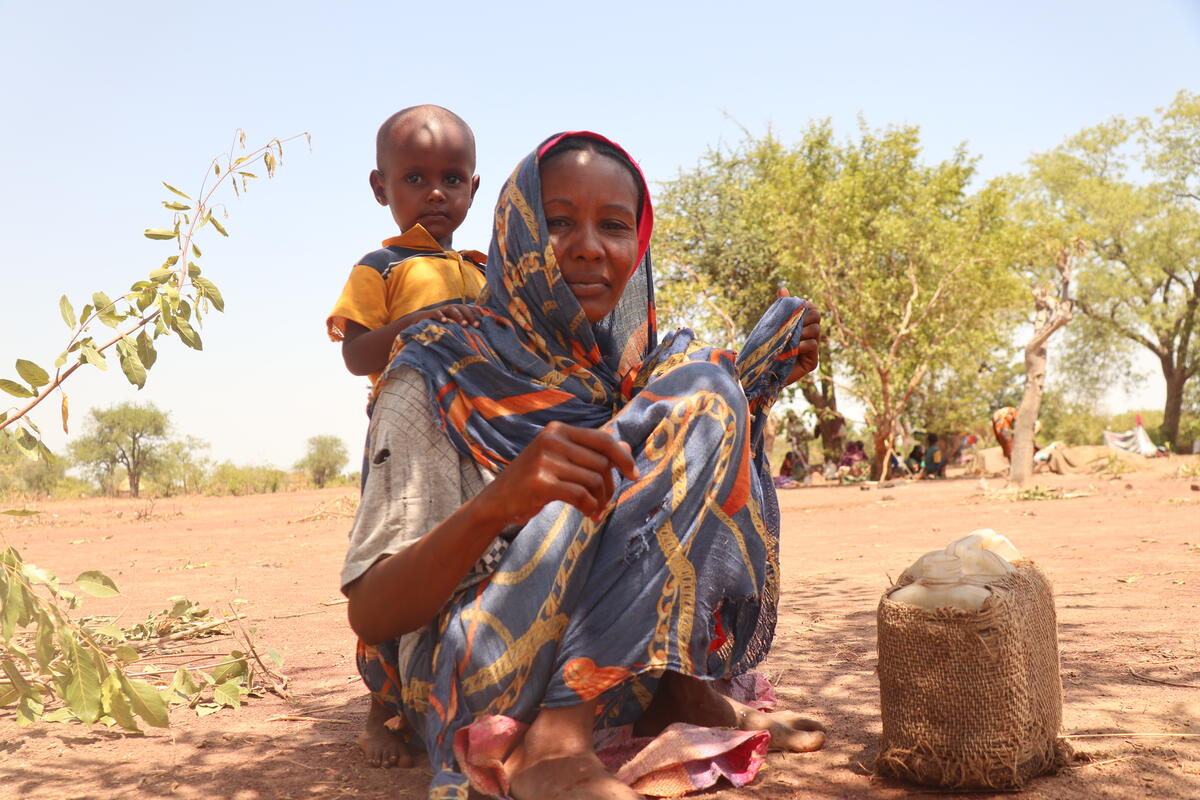 Sudanese mother crouched down with child, looking at the camera in a desert-like environment