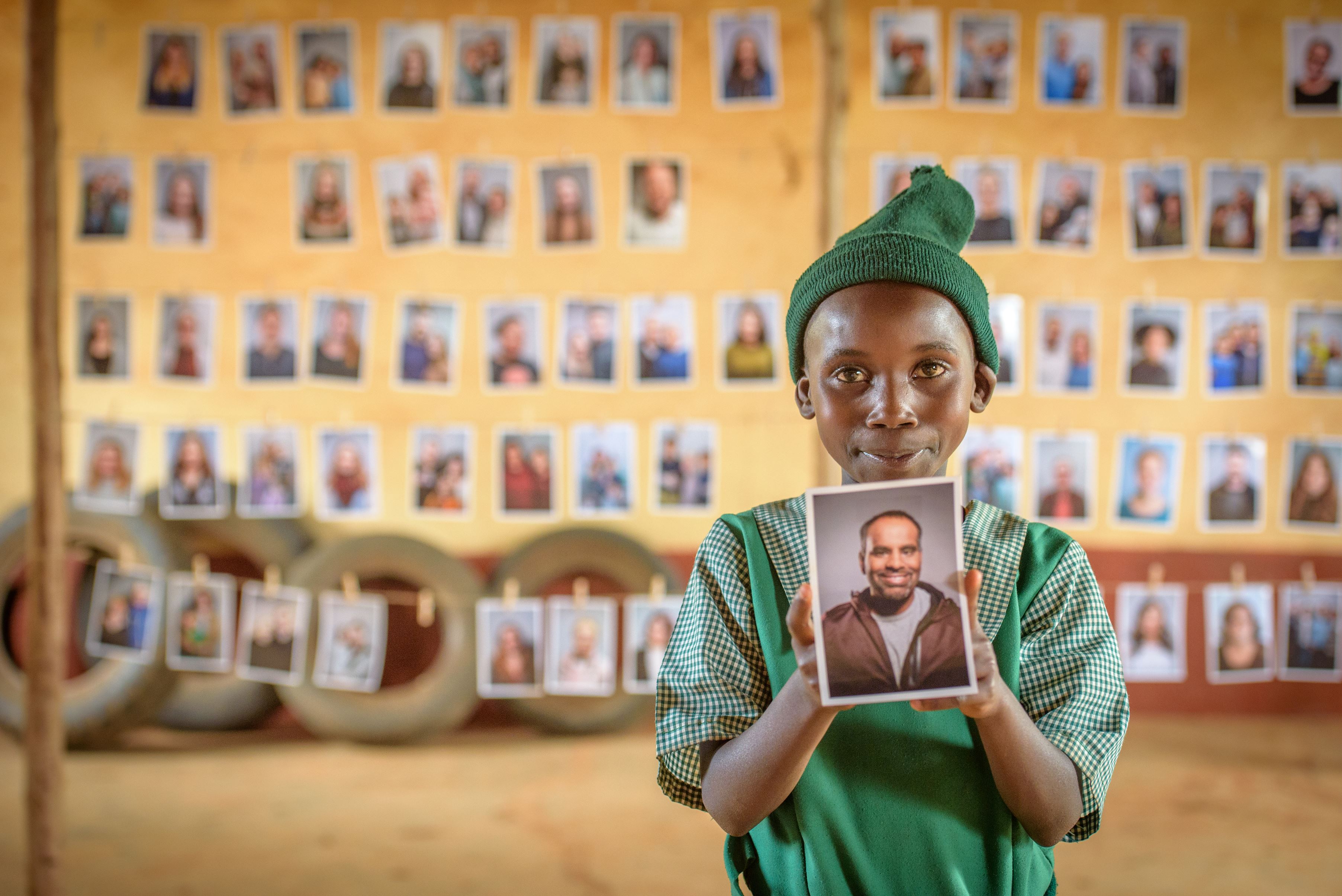 Girl in Kenya in a green dress holds a photo of the person she's chosen as her sponsor