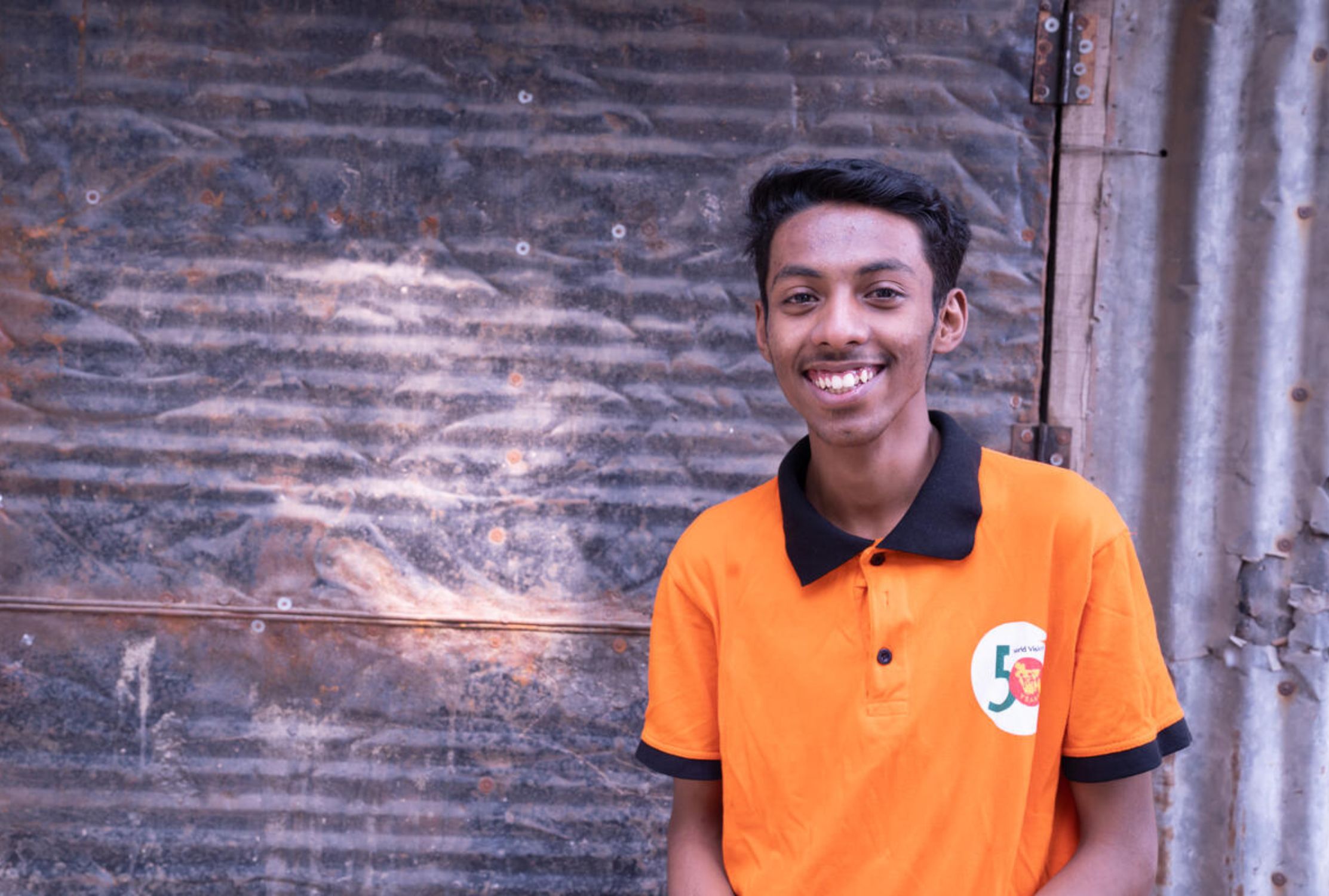 Teenage boy from Bangladesh smiling and wearing an orange World Vision polo shirt