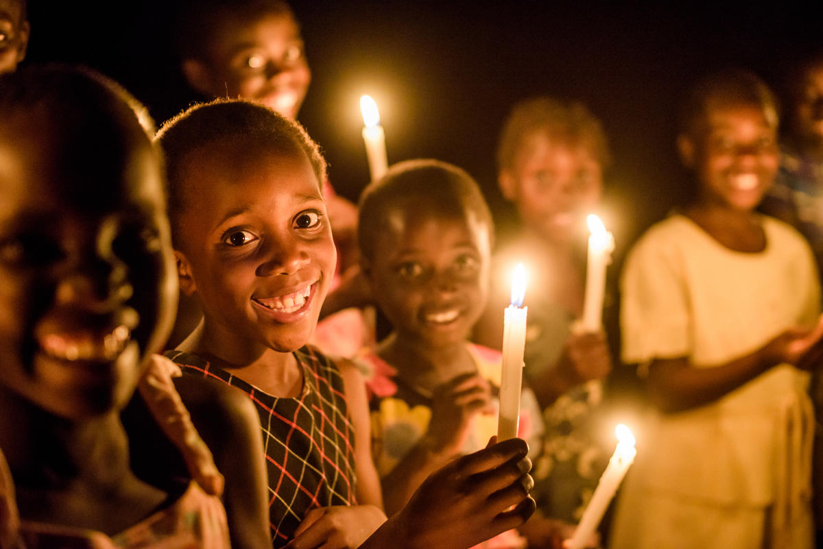 A group of children smile into the camera, standing in the dark in Zambia holding candles