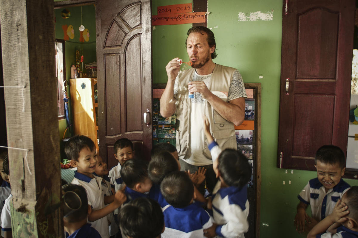 Jerome Flynn stands blowing bubbles surrounded by young children in Myanmar