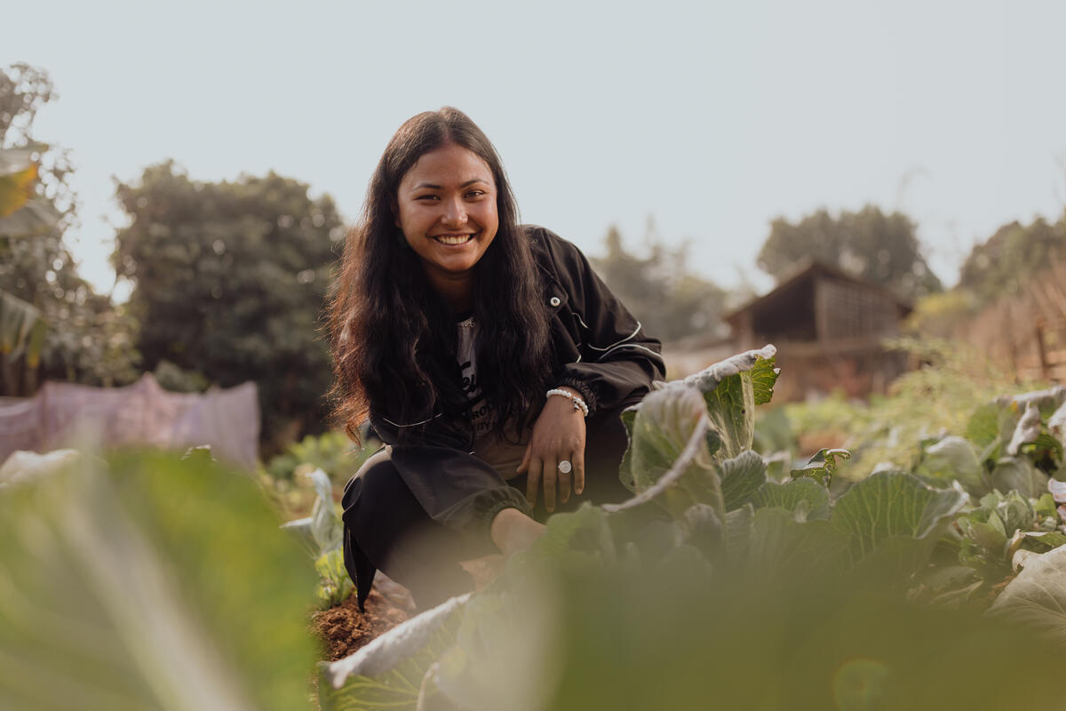 A girl in Nepal crouches within a field of produce. 