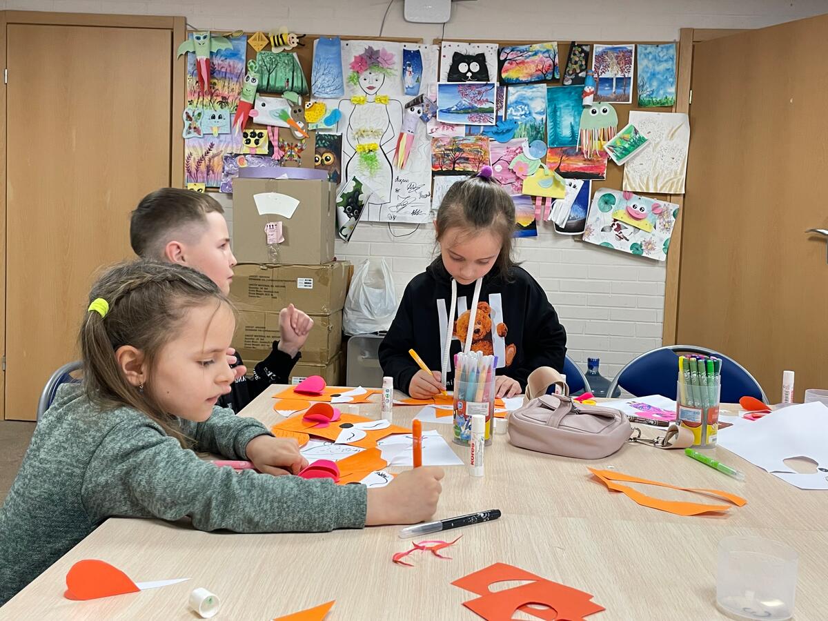 Three Ukrainian children doing crafts at a desk 