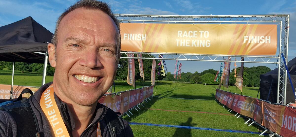Man poses for a selfie with his medal around his neck. There is a visible orange banner behind him.