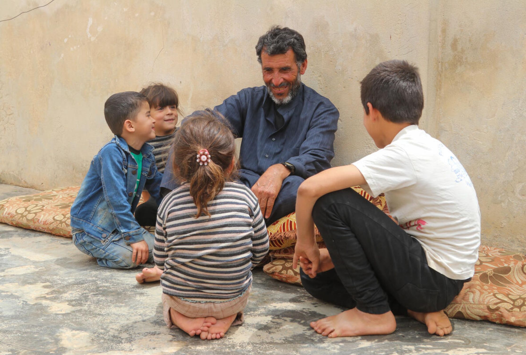 Syrian children sit around their grandfather who is smiling at them