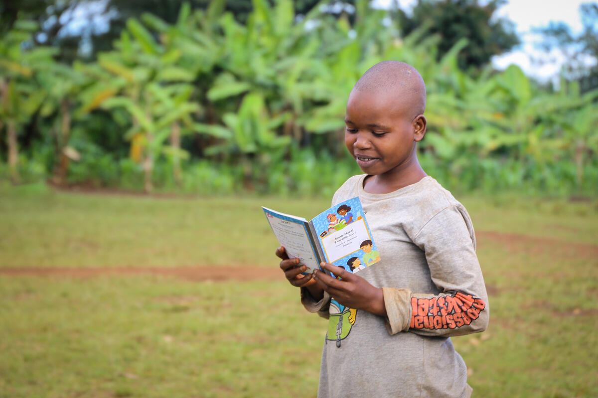 Child in Burundi looks at a picture or letter from their sponsor, standing outside in a field