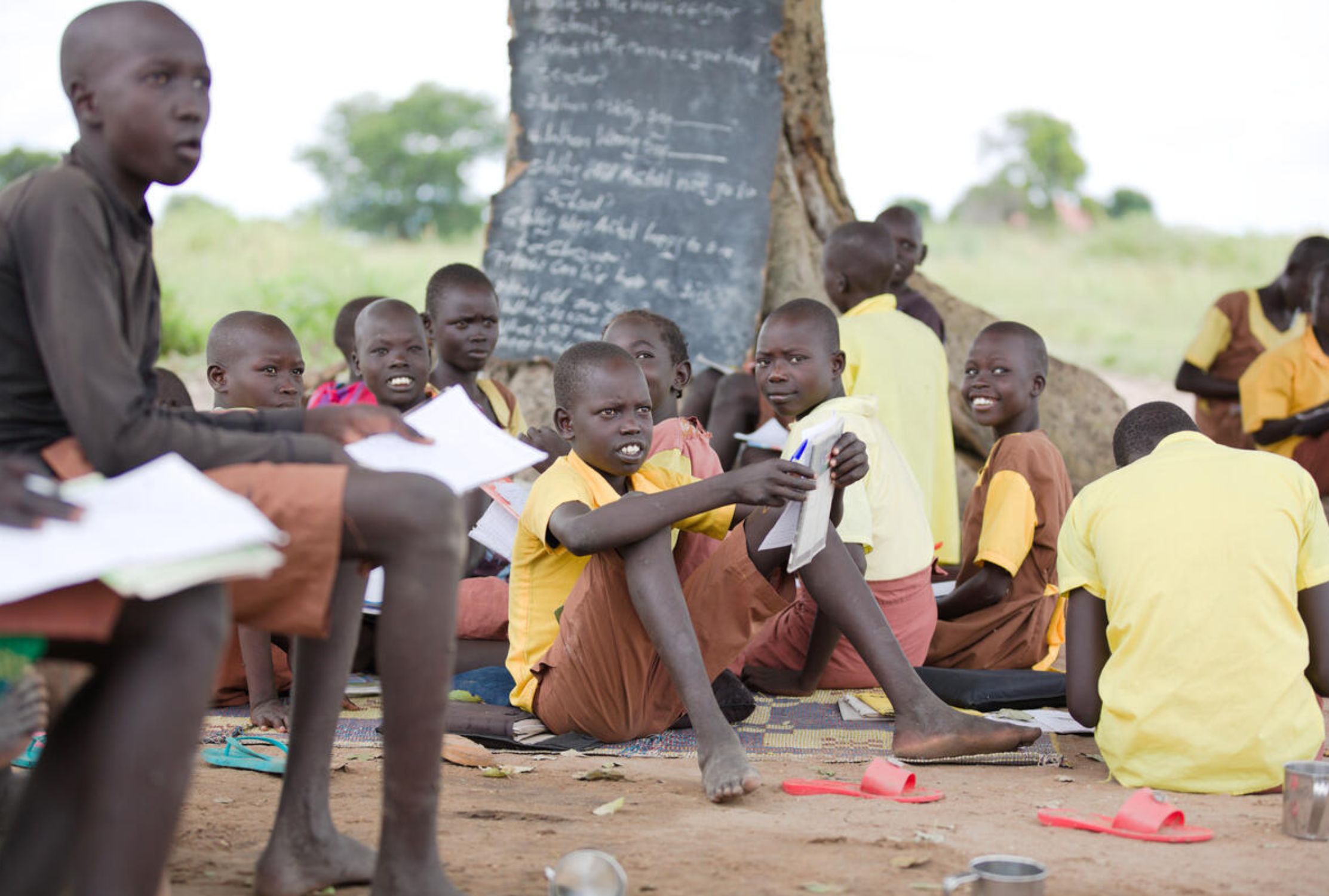 Boys from South Sudan sitting to learn on the floor of their outdoor primary school