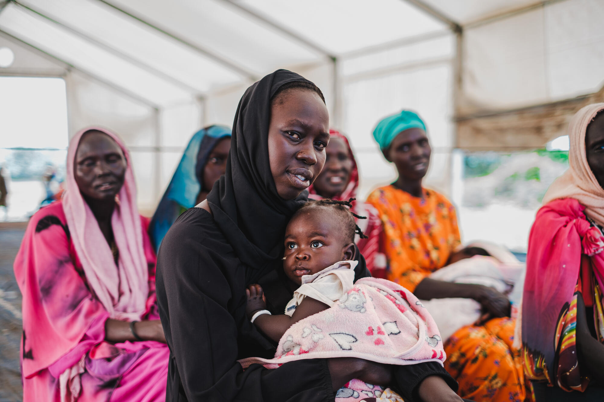 Women holding her child waits at a transit centre in South Sudan