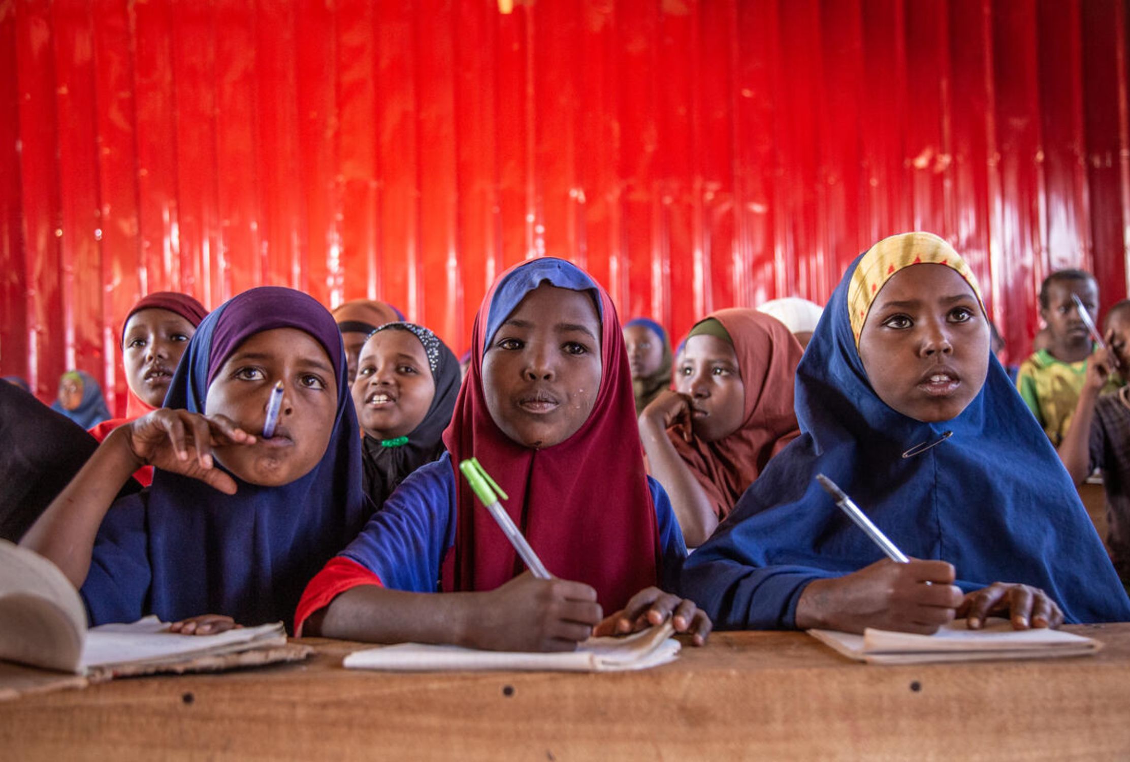 Three Somali girls learning in a classroom amongst peers