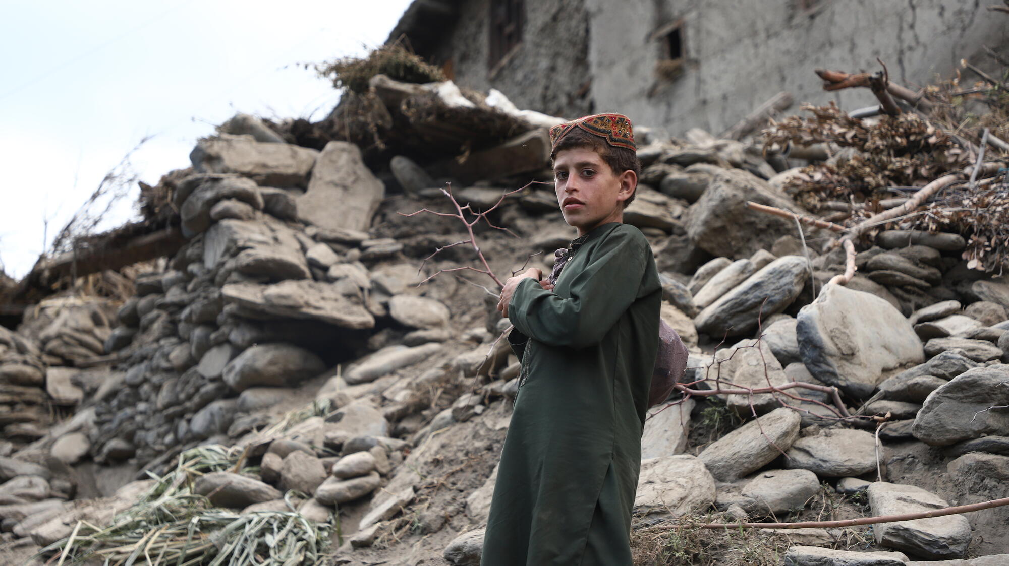 A boy stands in front of the wreckage of a building, destroyed by the earthquake in Afghanistan