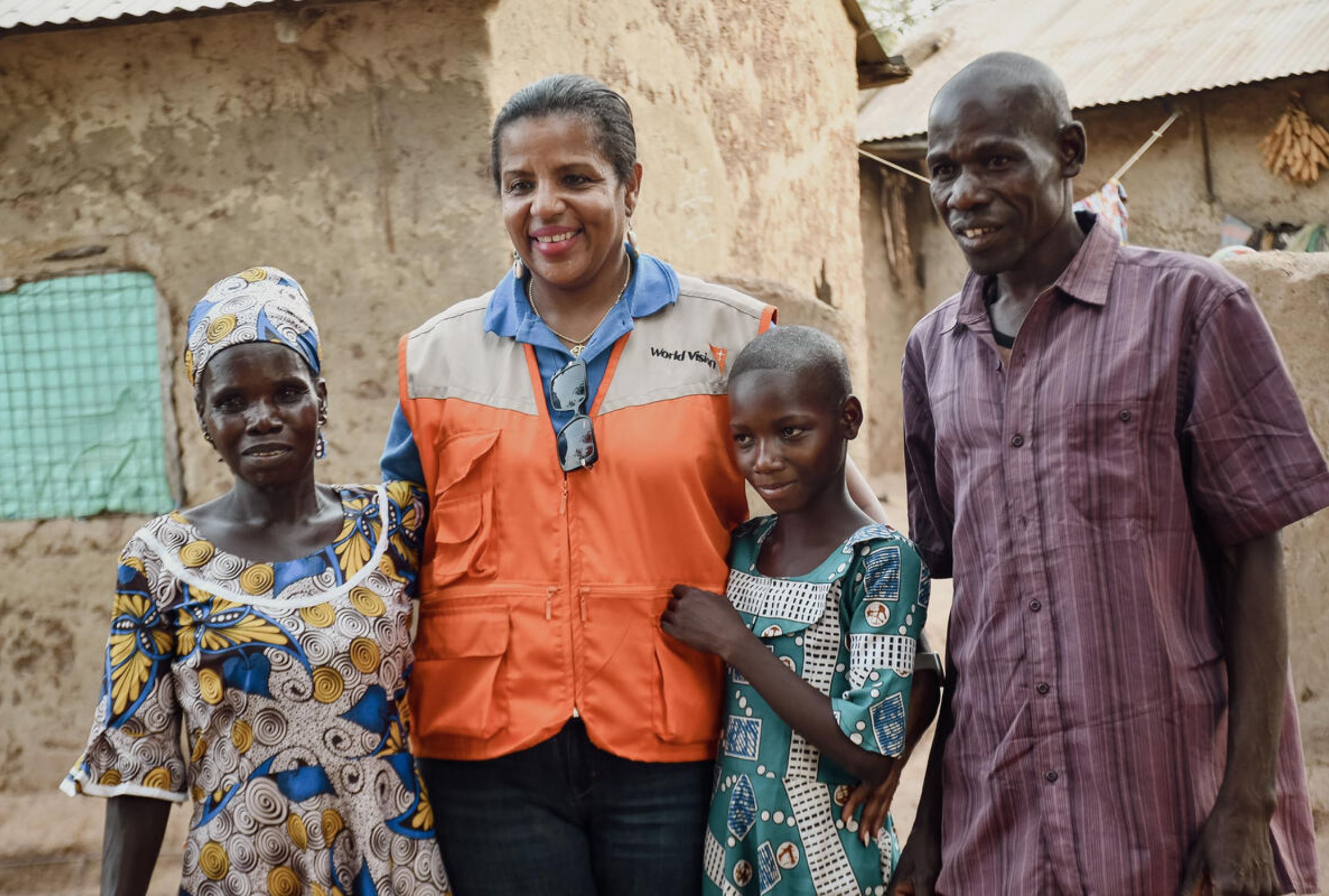 Ghanaian parents and daughter smiling with World Vision staff member who is wearing a branded vest
