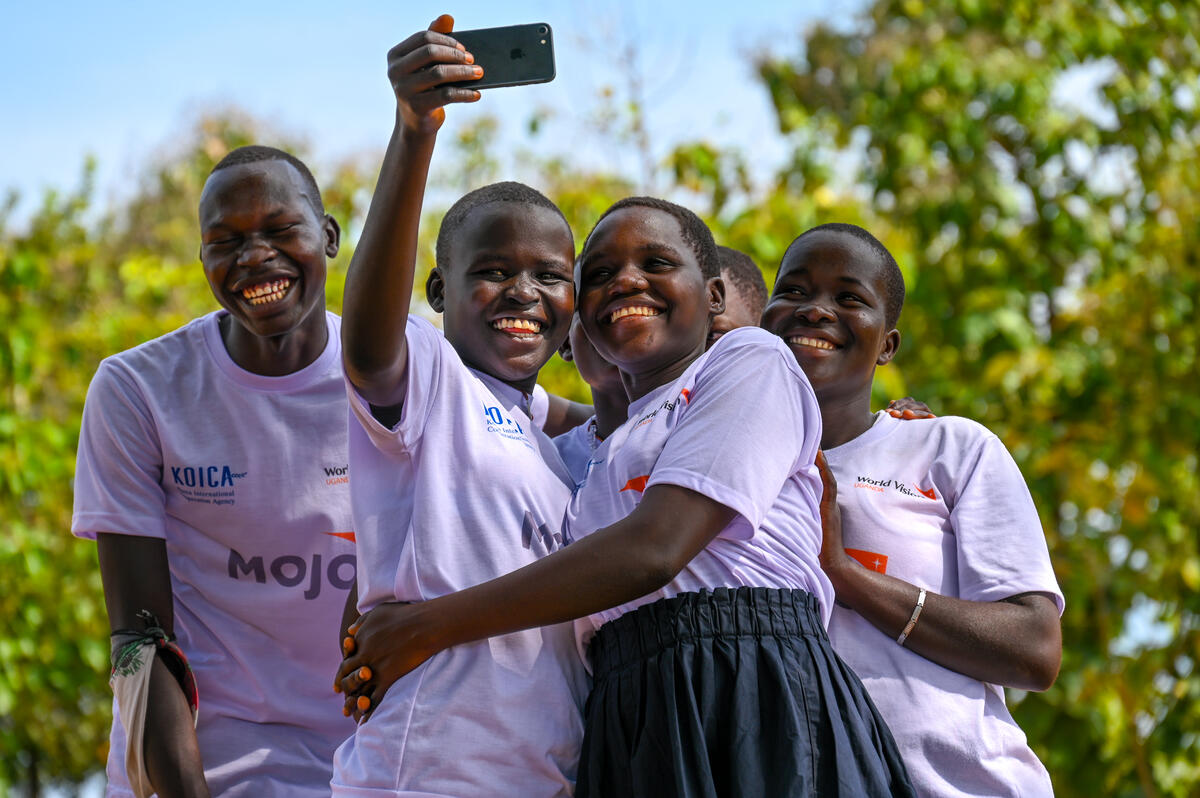 A crowd of teenager children in Uganda smile around a camera