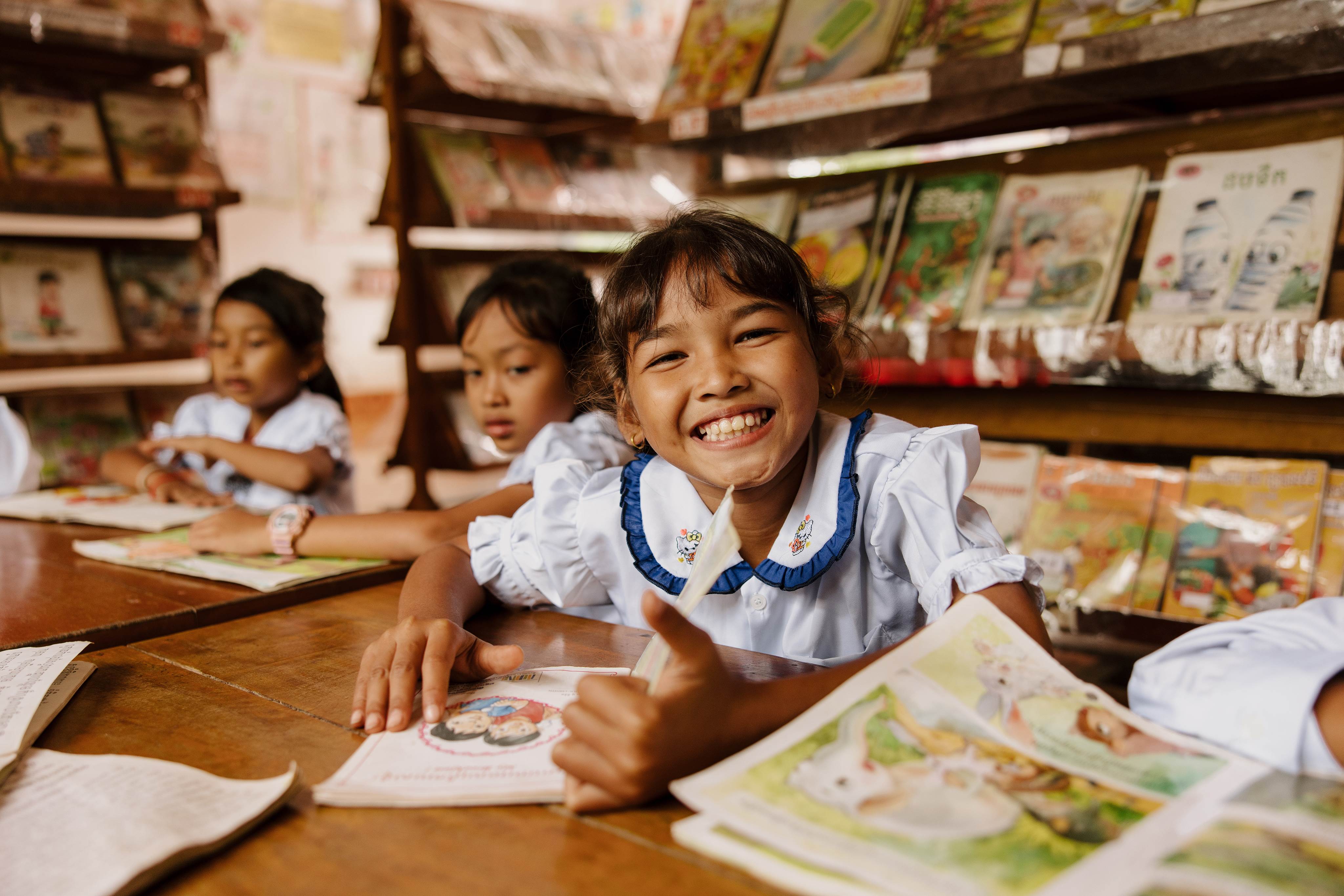 Girl from Cambodia in a school uniform sitting at a desk in a classroom and smiling at the camera