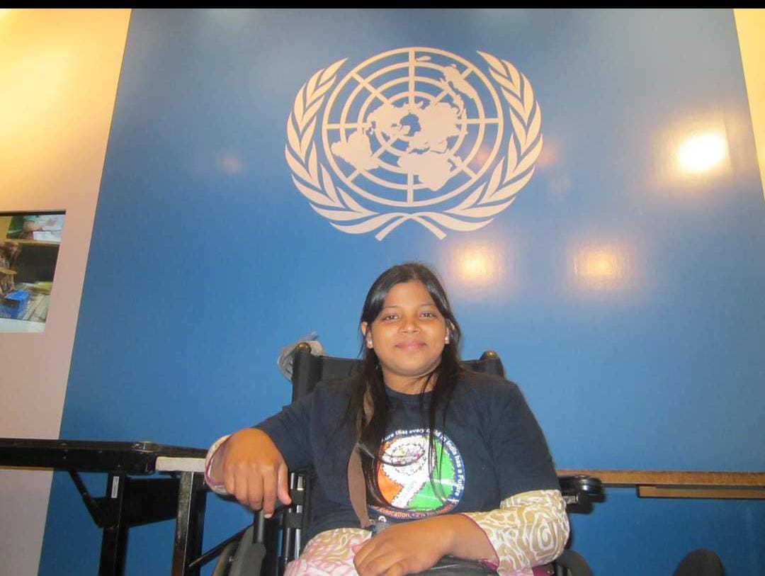 A girl smiles at the camera as she sits in her wheelchair, below the insignia of the UN