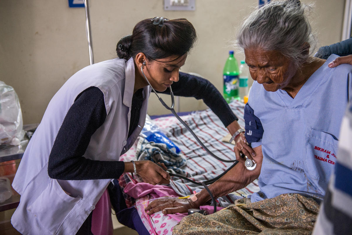 Amandeep checks on an elderly patient, holding stethoscope to her arm