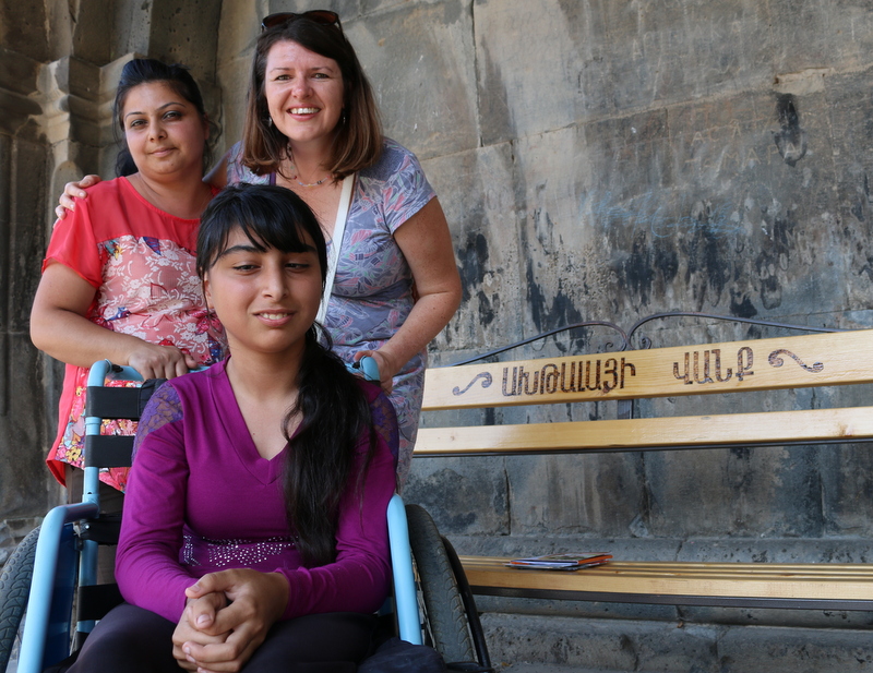 Girl in a wheelchair smiles, sitting in front of two older women in Armenia