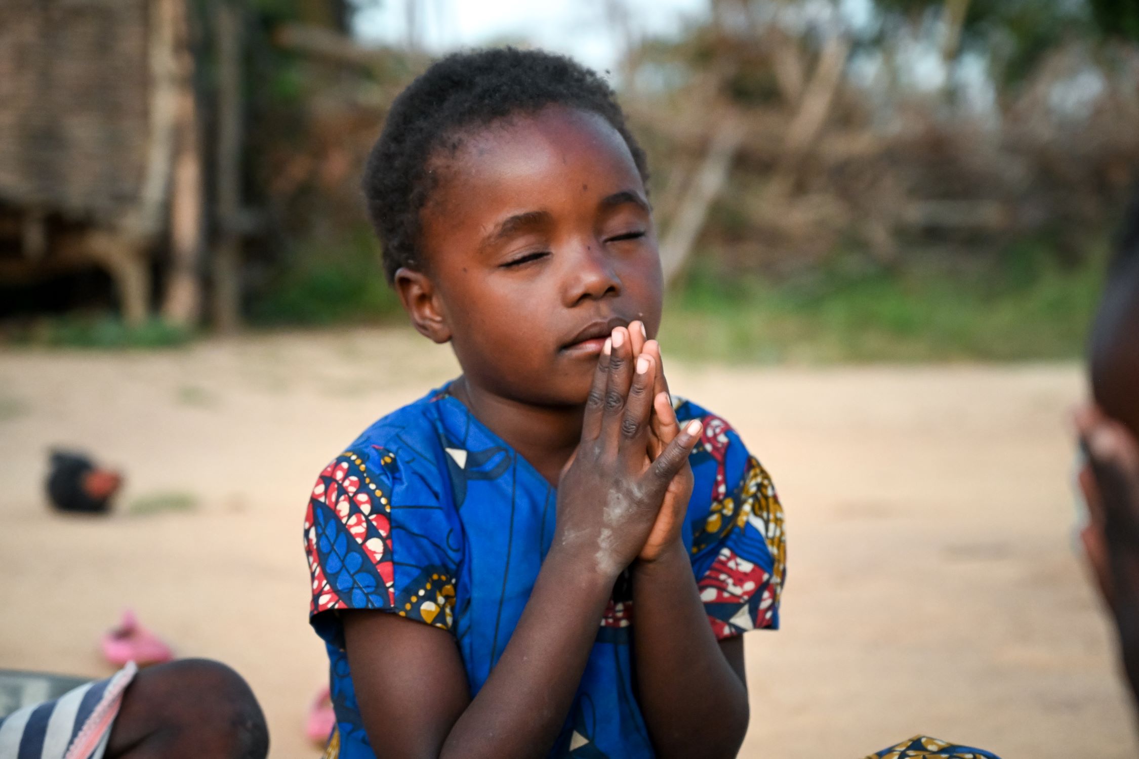 Young Zambian girl with eyes shut and hands together in prayer position