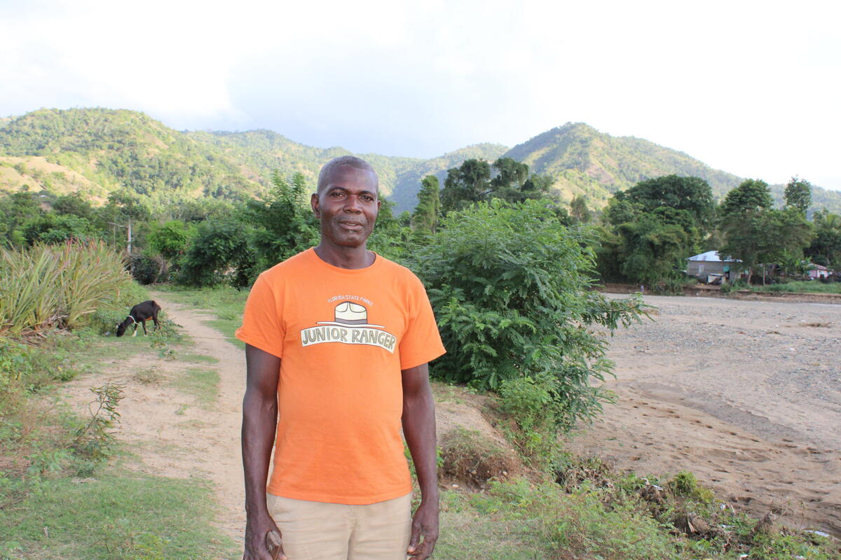 Haitian farmer standing in a field, with Haiti's mountainous terrain in the background
