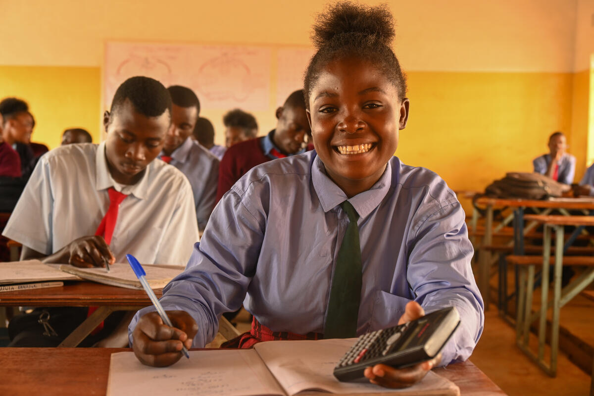 A girl in Zambia sits at a desk in the front of a classroom.