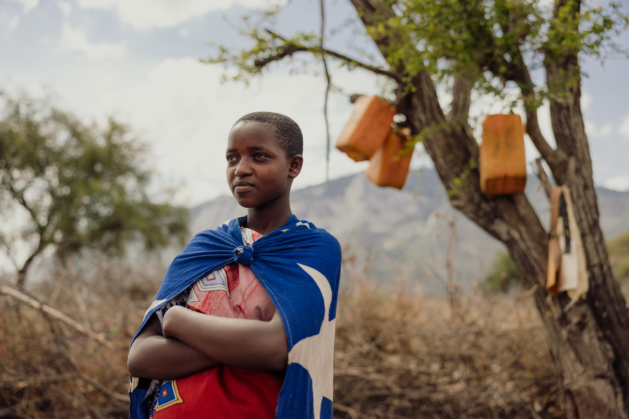 A child standing outside in a rural setting, arms crossed, looking into the distance