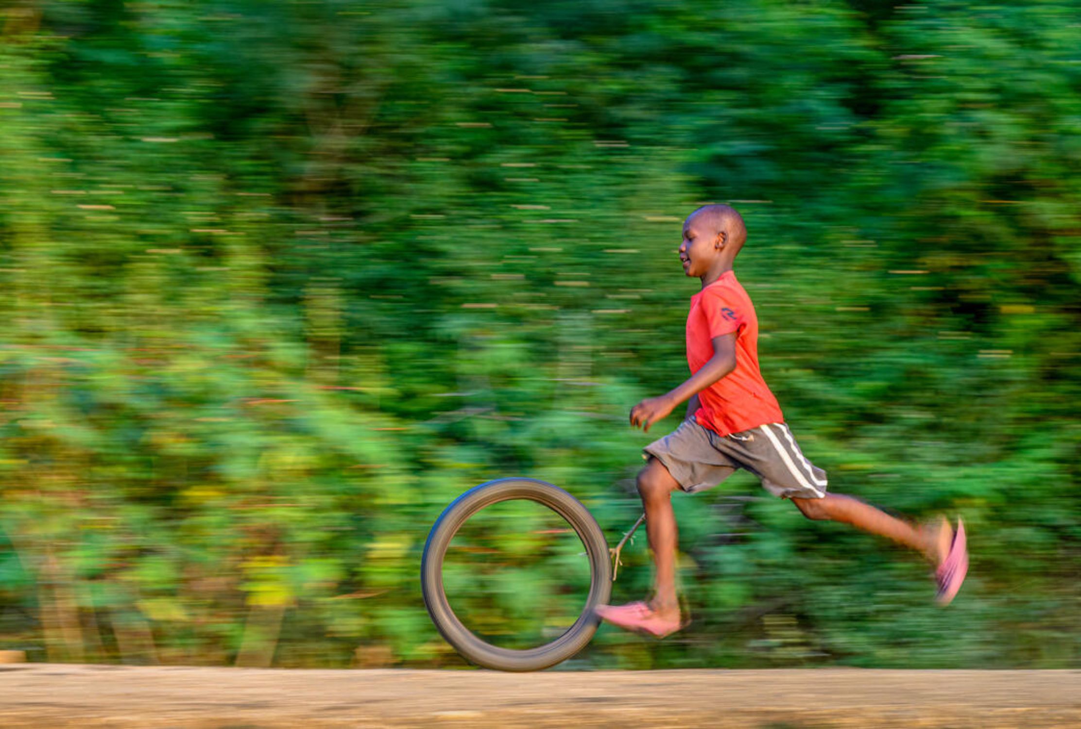 Kenyan boy plays by pushing his hoop on the road 