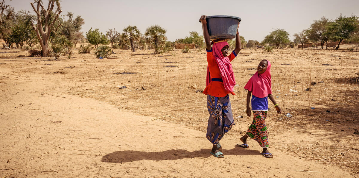 Two young girls from Niger walking and one holding a water bucket on her head