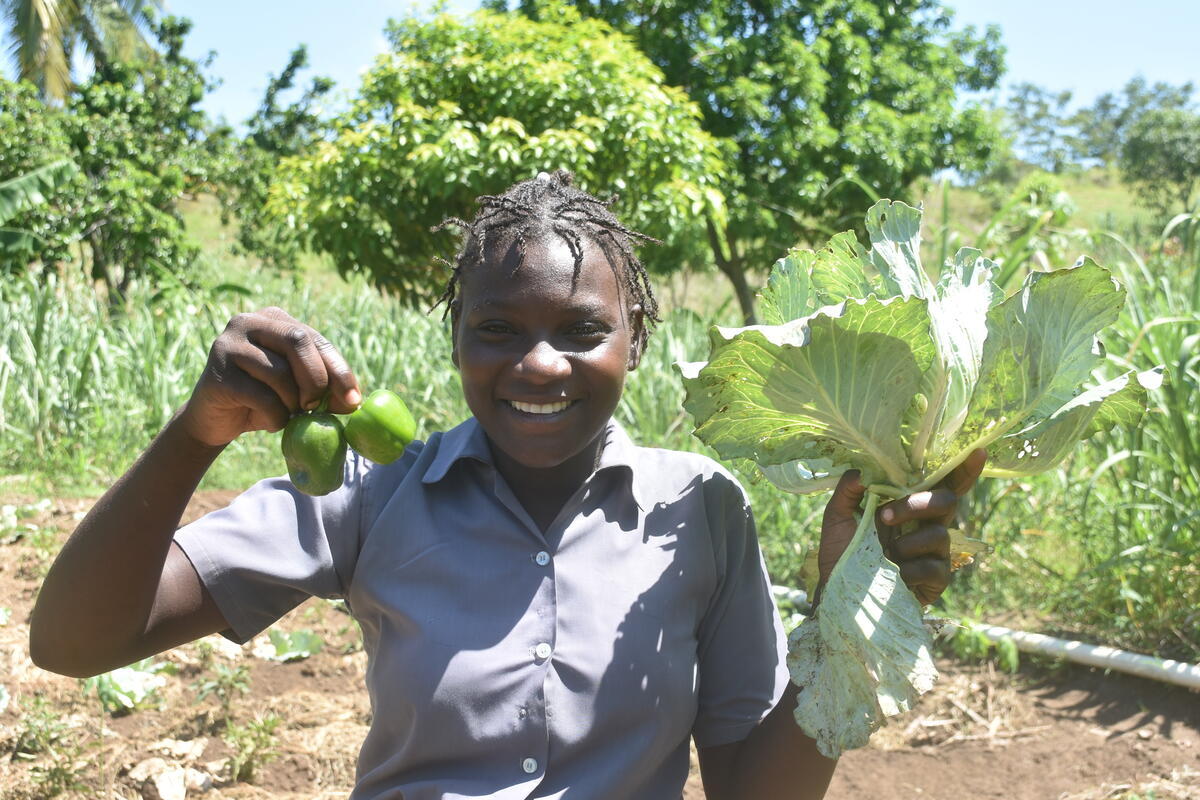 Rosekamène stands in a farm holding harvested crops and smiling.