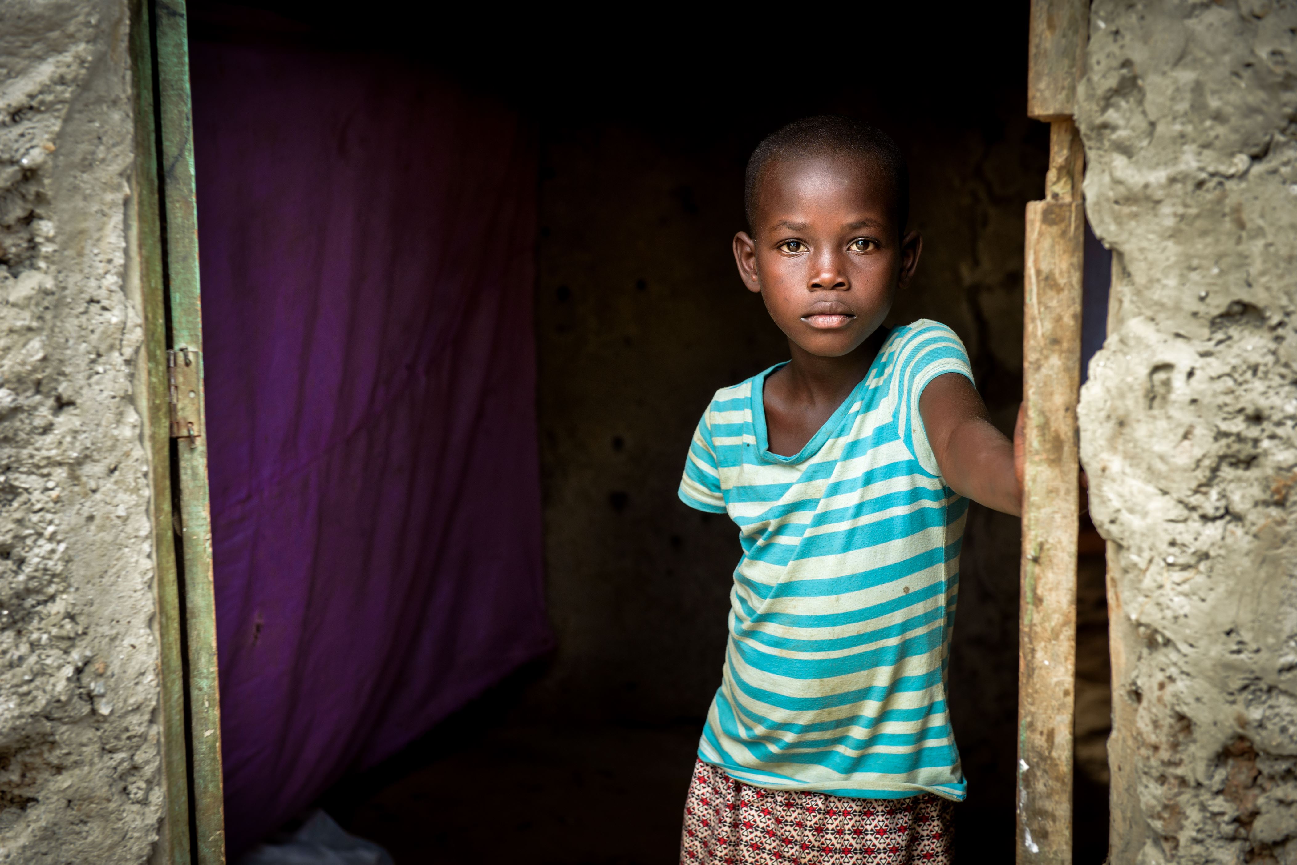 Serious 8-year-old girl stands in the doorway of her family's small 2-room home