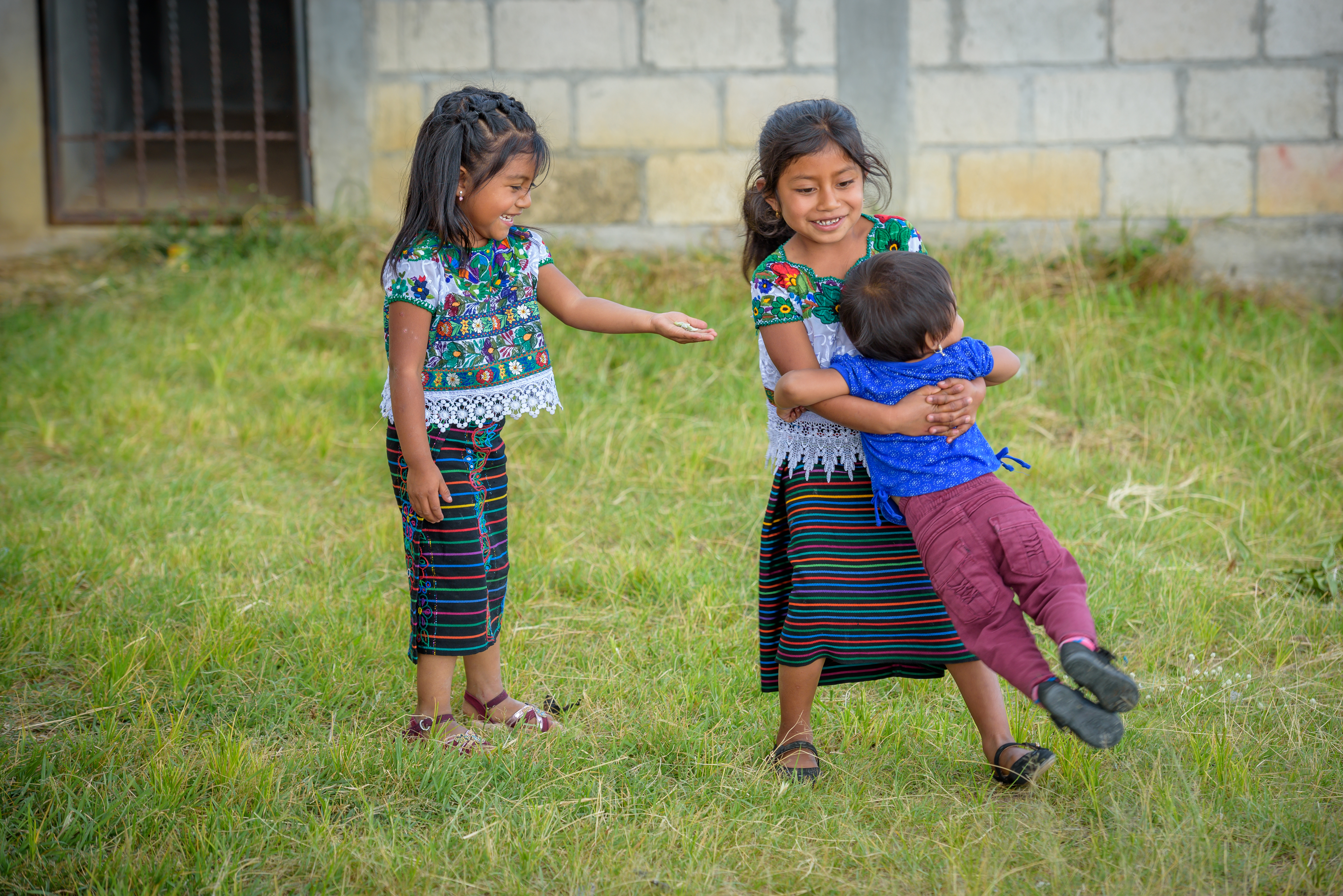 A girl twirls a younger child round in Guatemala, whilst another girl points and smiles at the fun