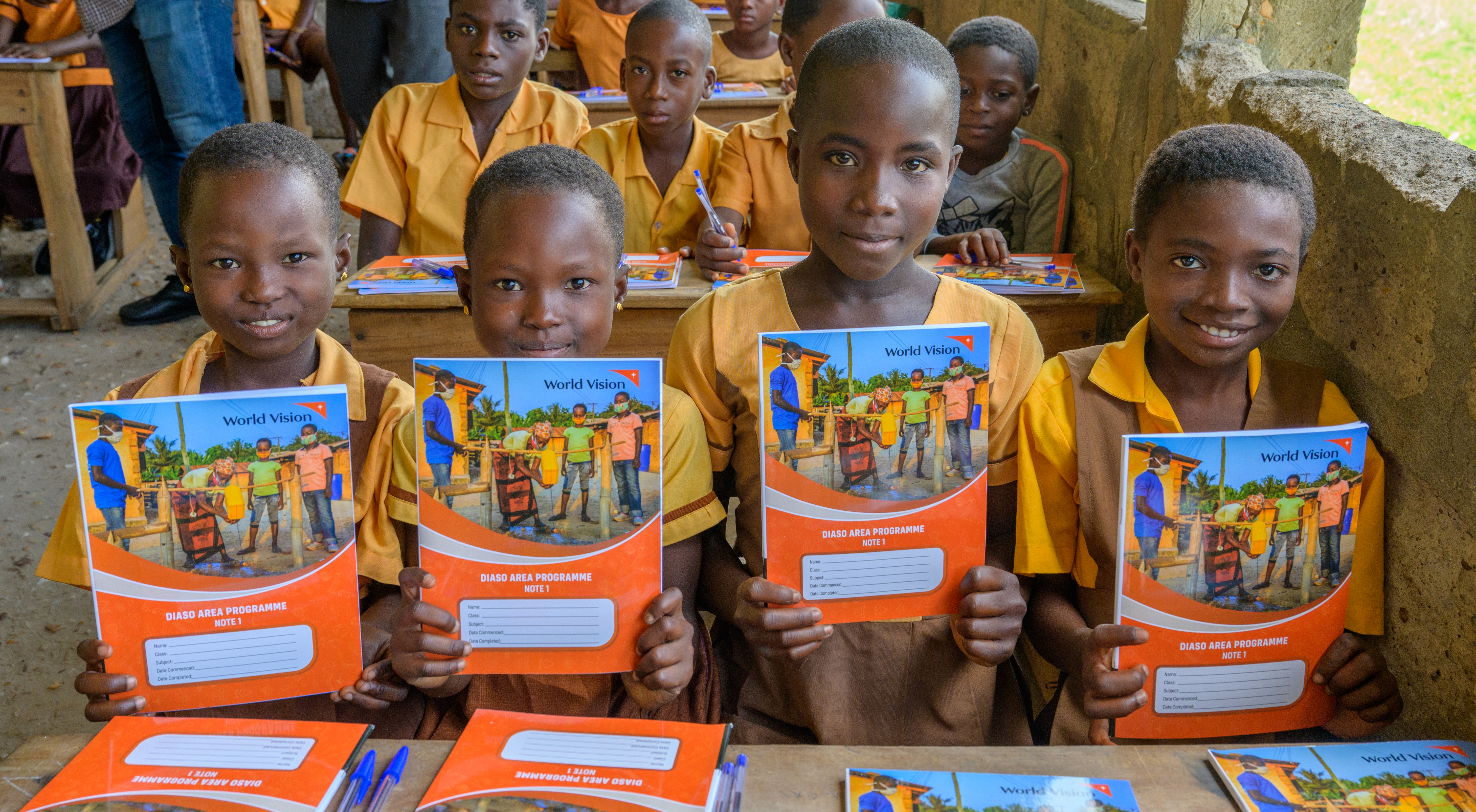 Four girls sat a a school desk in Ghana, holding books provided by World Vision supporters donations