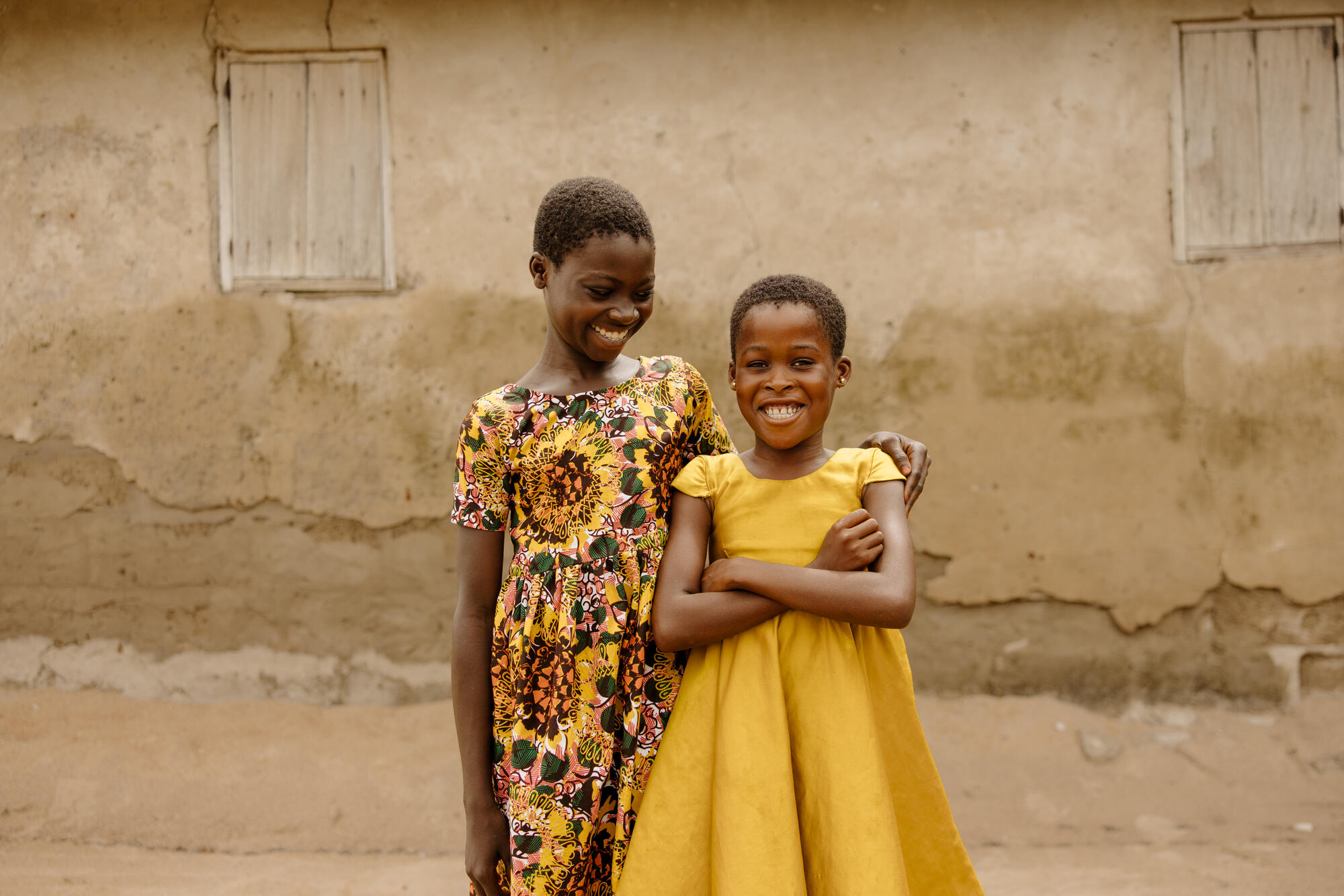 Two young girls in Ghana pose for a picture outside of their kids club building.