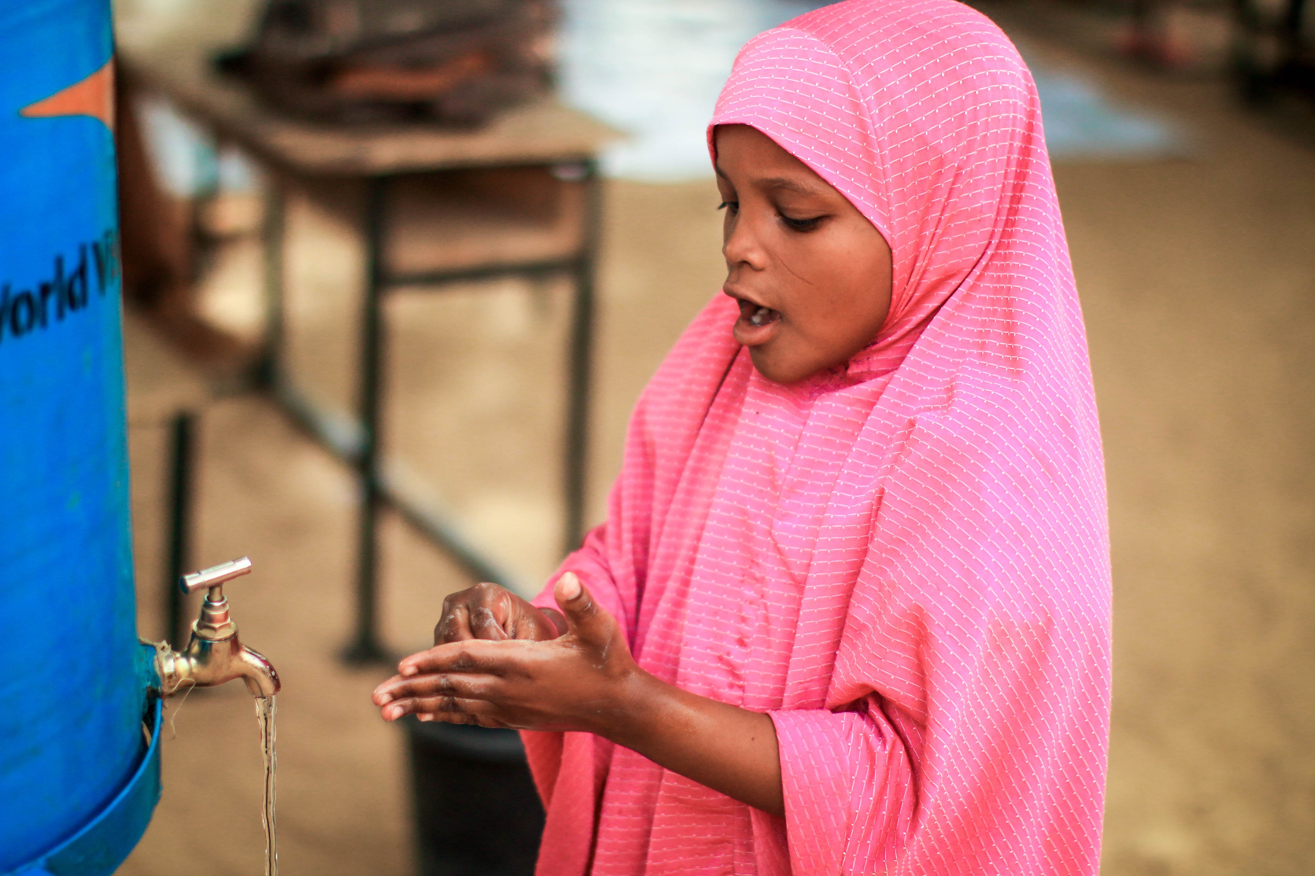 Girl in Niger wearing pink washes her hands next to a water dispenser