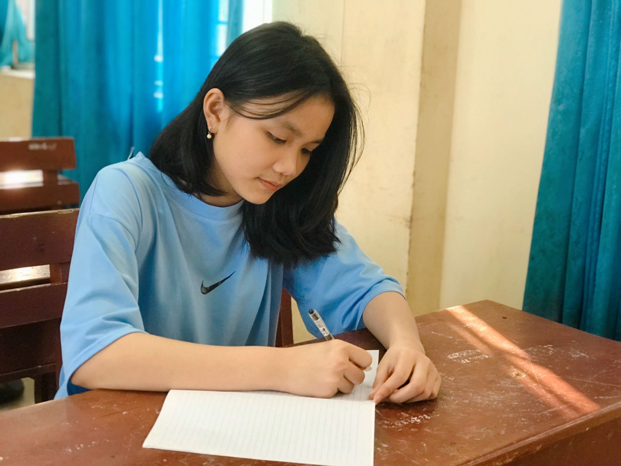 Teenage girl from Vietnam writing on lined paper while sat at a desk