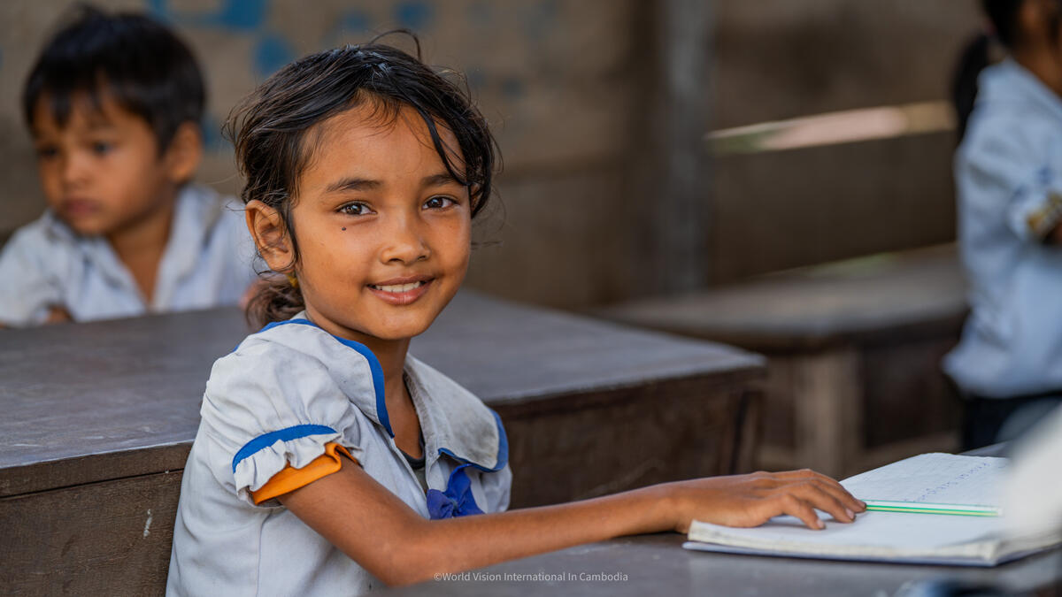 Cambodian school girl sits at a desk smiling in school uniform