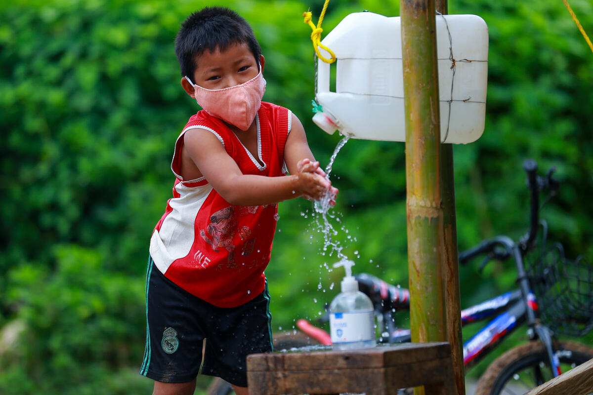 Child in Myanmar wears a face mask and cleans her hands in a tippy tap