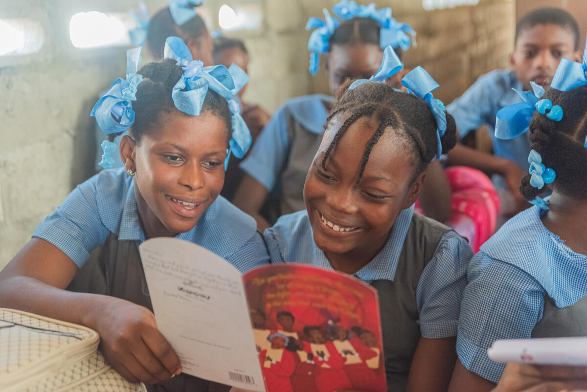 A young girl from Haiti sat in a classroom with a workbook, with lots of other children in the background