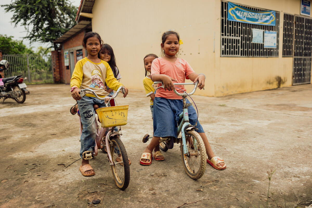 Two young girls pose on their bicycles with their siblings behind them