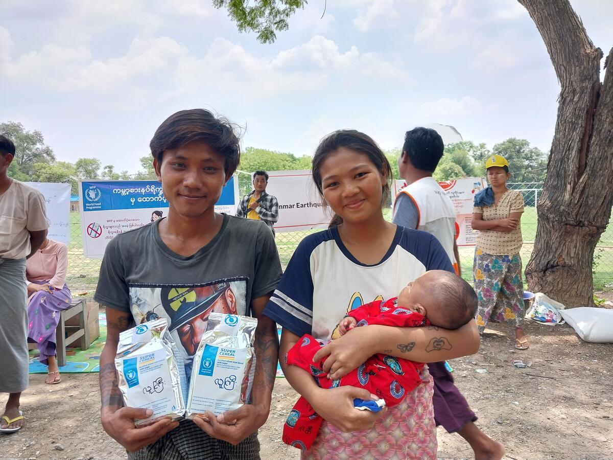 A young man holds food supplies with a young mother holding her baby