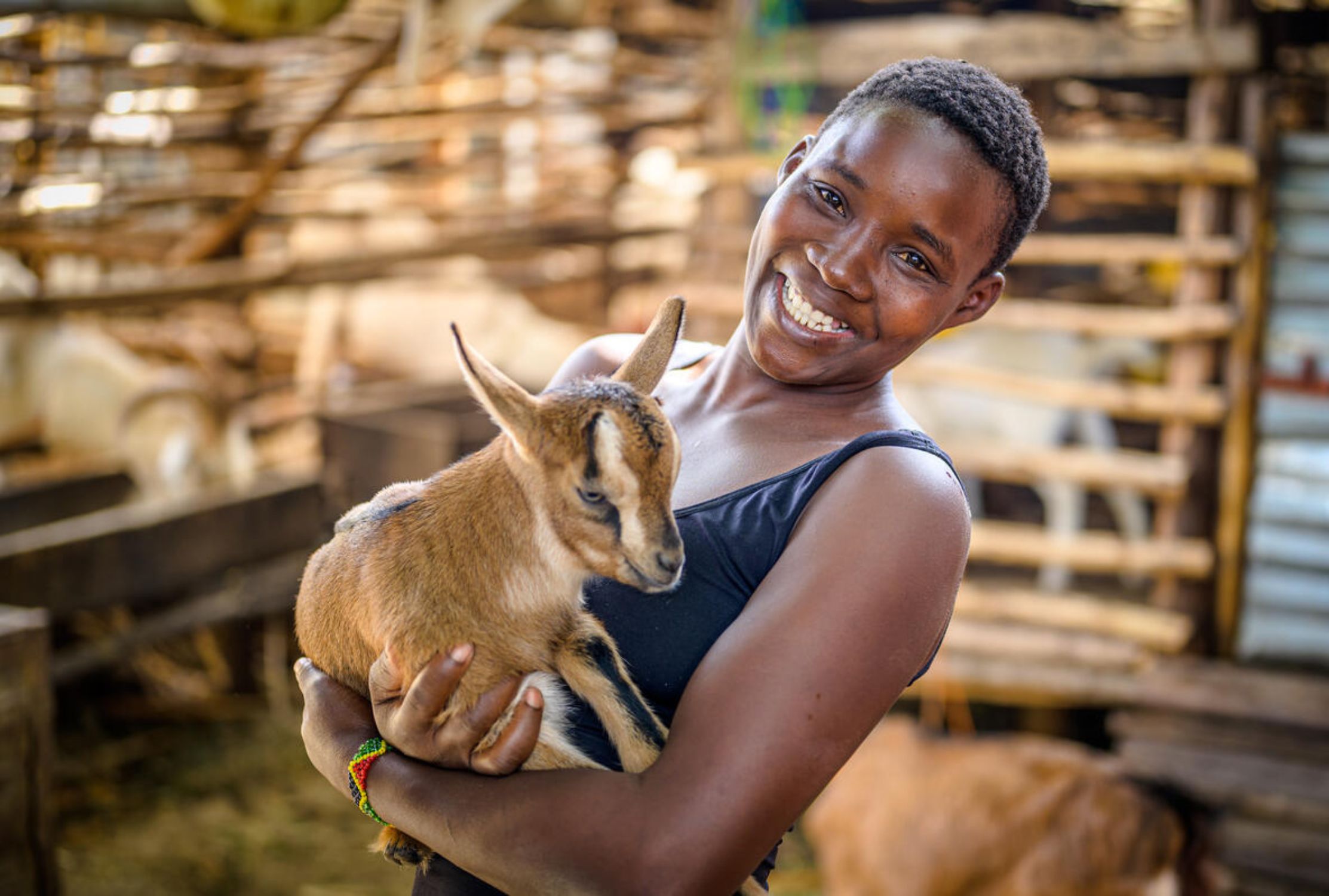 A girl looks at the camera smiling while holding a goat