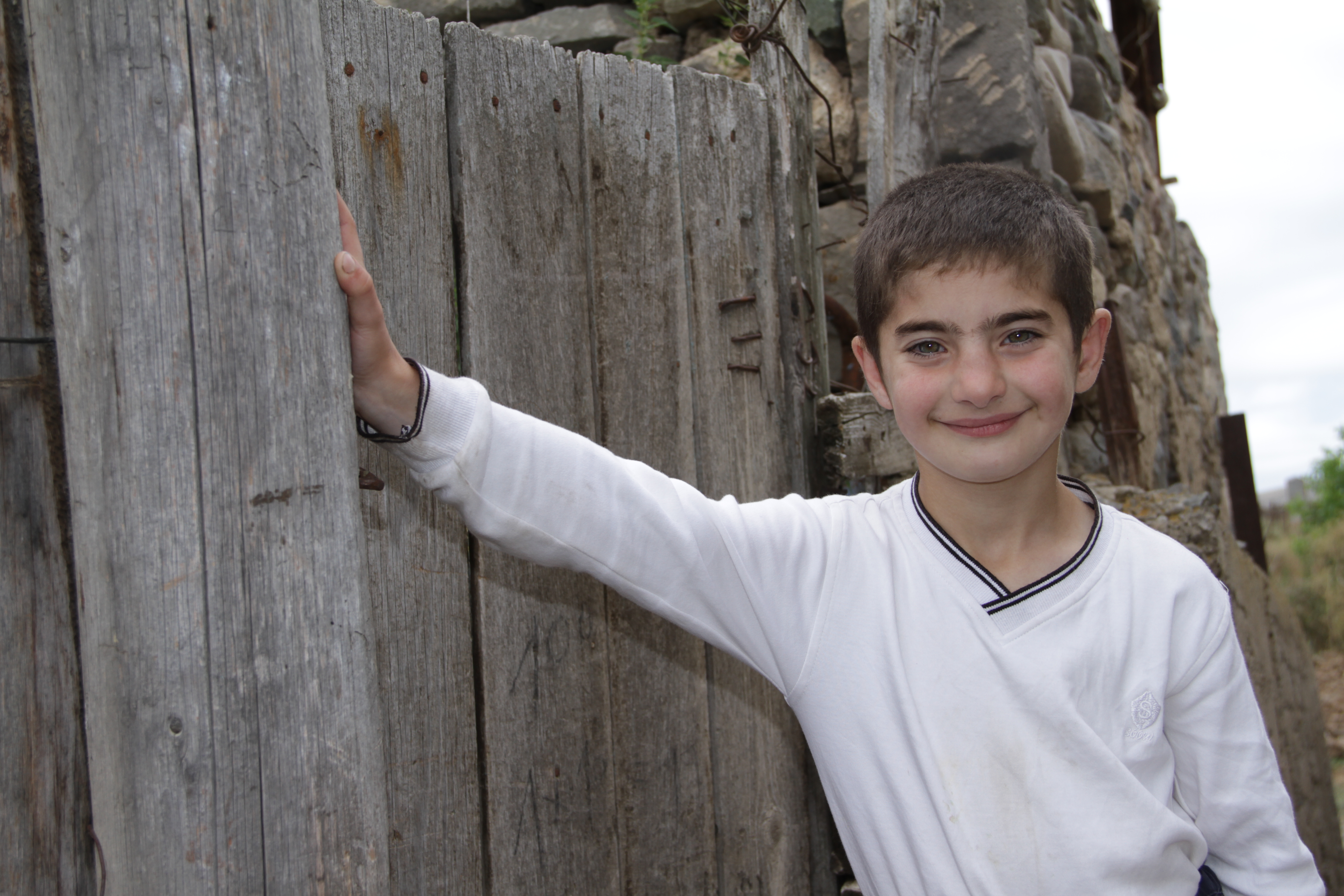 Armenian boy leans an arm against a wall and smiles for the camera